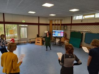 Nascholing muziek - Iemand geeft een zangles aan docenten in een gymlokaal